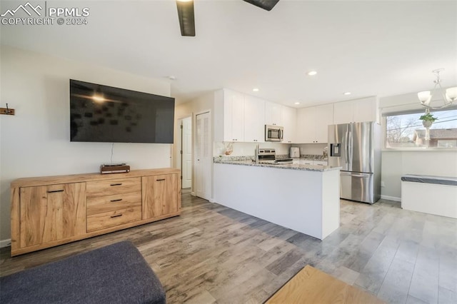 kitchen with light stone counters, stainless steel appliances, pendant lighting, light hardwood / wood-style flooring, and white cabinetry