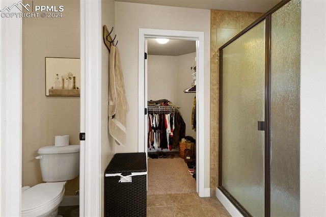 full bathroom with toilet, a shower stall, a walk in closet, and tile patterned flooring