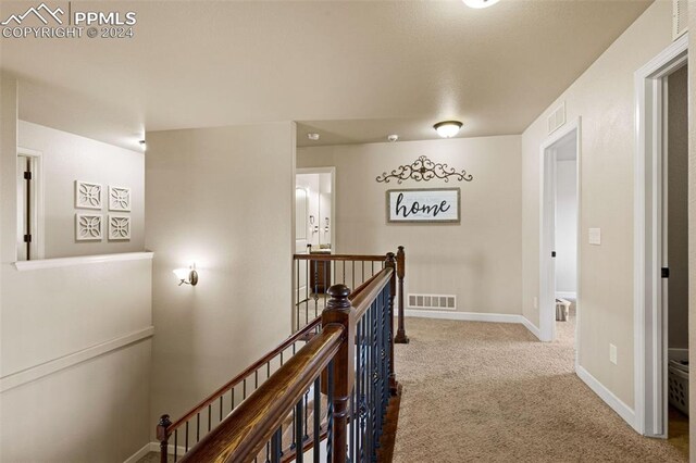 hallway with carpet floors, baseboards, visible vents, and an upstairs landing