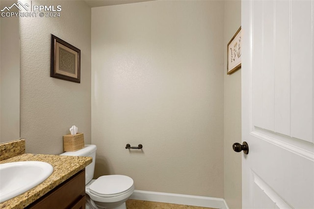 half bath with baseboards, vanity, and toilet