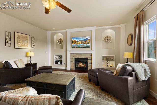 living area featuring a ceiling fan, a glass covered fireplace, dark wood finished floors, and baseboards