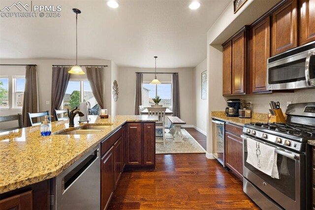 kitchen featuring plenty of natural light, dark wood finished floors, appliances with stainless steel finishes, light stone countertops, and pendant lighting