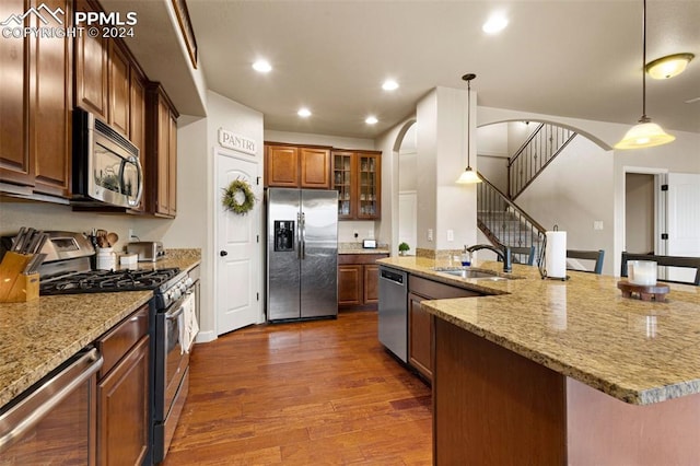 kitchen with arched walkways, stainless steel appliances, dark wood-style flooring, hanging light fixtures, and glass insert cabinets