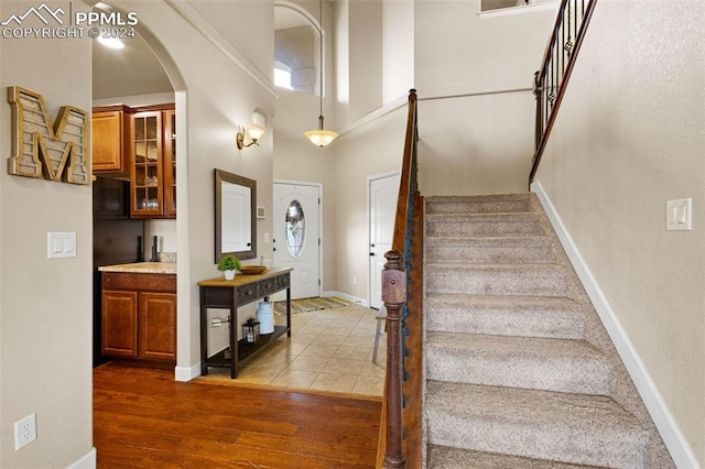 foyer featuring arched walkways, a high ceiling, wood finished floors, baseboards, and stairway