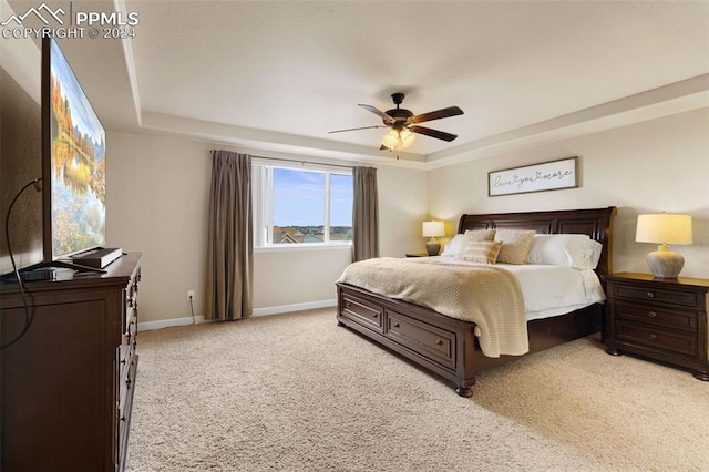 bedroom with light carpet, baseboards, a raised ceiling, and a ceiling fan