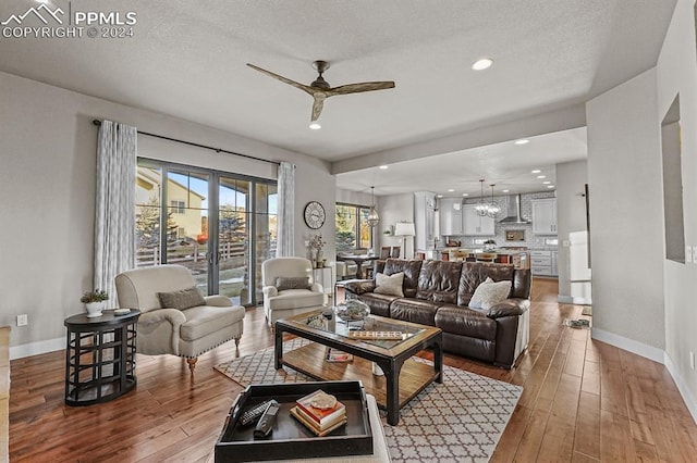 living room featuring wood-type flooring, ceiling fan with notable chandelier, and a textured ceiling