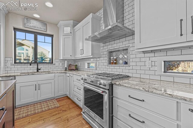 kitchen with sink, light hardwood / wood-style flooring, high end range, white cabinetry, and wall chimney exhaust hood