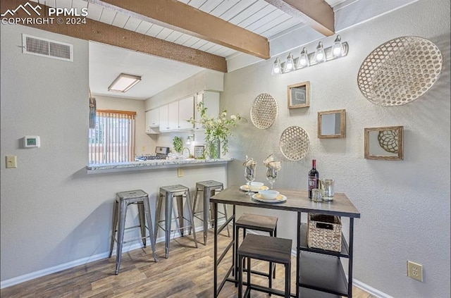 kitchen featuring kitchen peninsula, stainless steel range, beam ceiling, white cabinets, and hardwood / wood-style floors