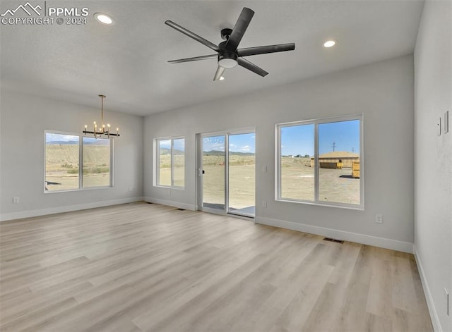 empty room with ceiling fan with notable chandelier, light wood-type flooring, and a wealth of natural light