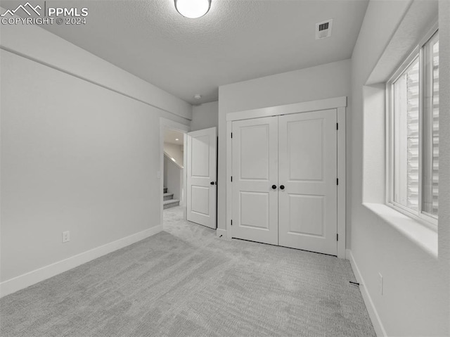 unfurnished bedroom featuring a textured ceiling, light colored carpet, and a closet