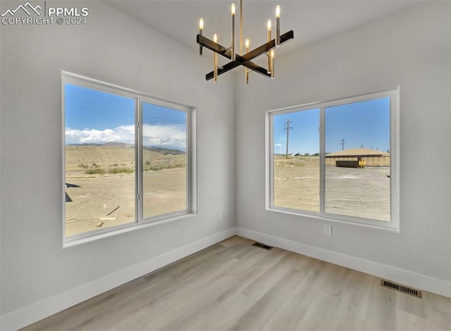 empty room with light wood-type flooring and a notable chandelier