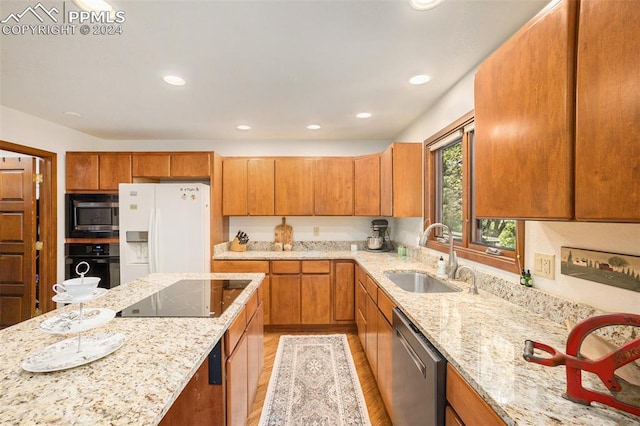 kitchen with light wood-type flooring, light stone counters, black appliances, and sink