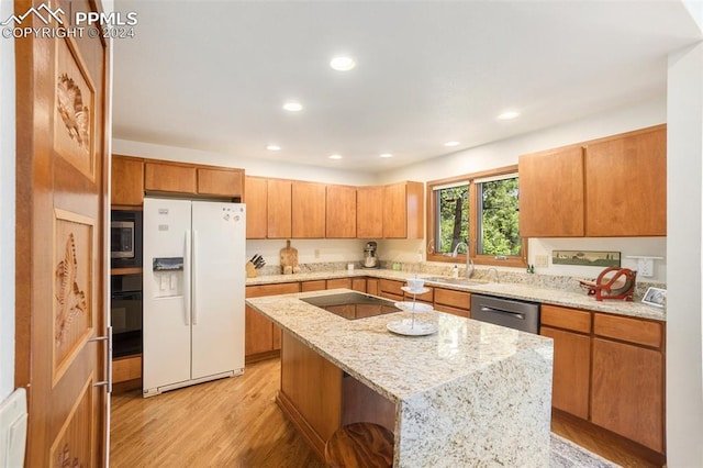 kitchen featuring light stone counters, sink, black appliances, light hardwood / wood-style flooring, and a kitchen island