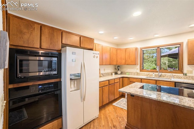 kitchen featuring light stone counters, sink, black appliances, and light wood-type flooring