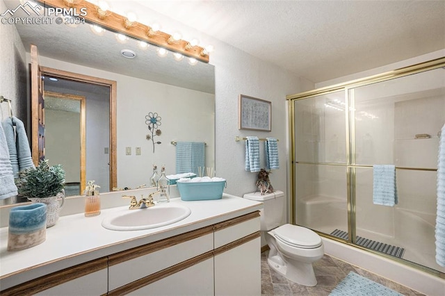 bathroom featuring vanity, toilet, a shower with shower door, and a textured ceiling