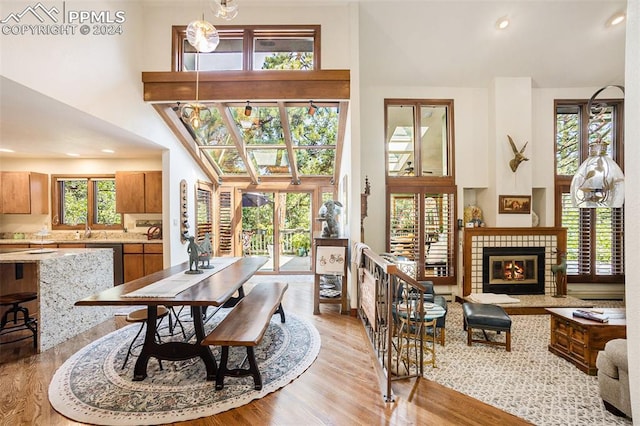 dining area featuring a tiled fireplace, light hardwood / wood-style flooring, a towering ceiling, and sink