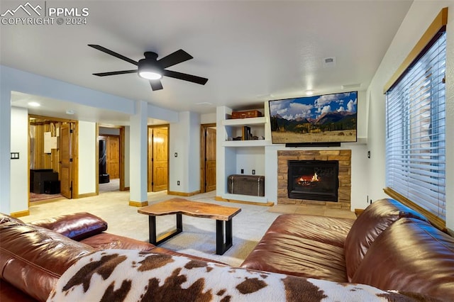 carpeted living room with a stone fireplace and ceiling fan