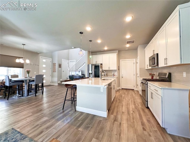 kitchen with white cabinets, stainless steel appliances, hanging light fixtures, and a kitchen island with sink