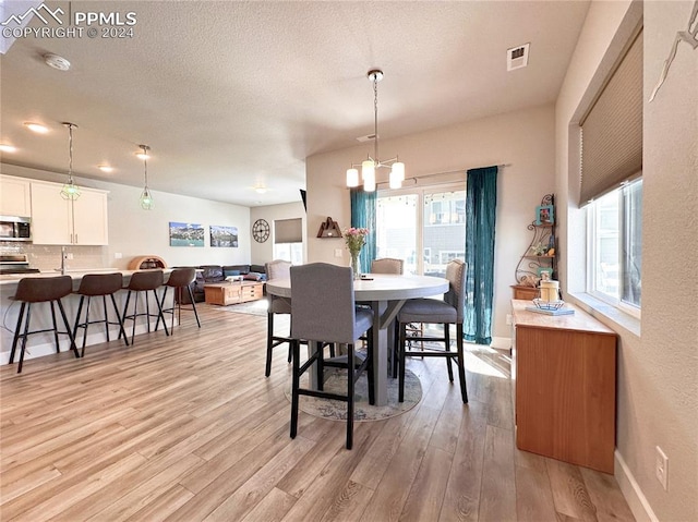 dining room with light wood-type flooring, a textured ceiling, and an inviting chandelier