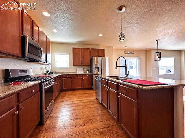 kitchen featuring decorative light fixtures, a center island with sink, stainless steel appliances, light wood-style flooring, and a sink