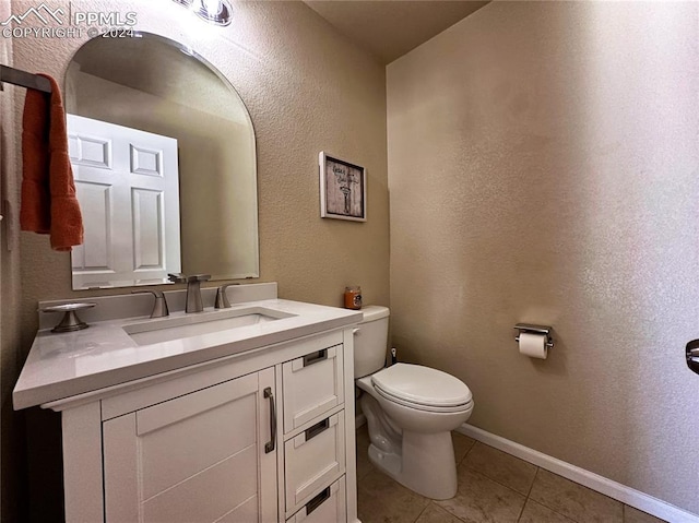 half bathroom with a textured wall, toilet, vanity, baseboards, and tile patterned floors