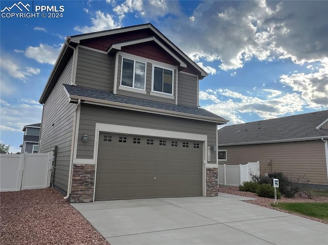 craftsman-style home with a garage, stone siding, fence, and concrete driveway