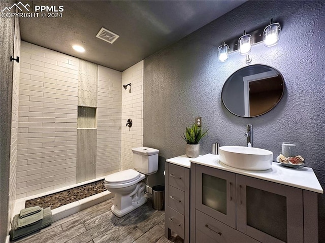 bathroom featuring visible vents, a textured wall, toilet, wood tiled floor, and tiled shower