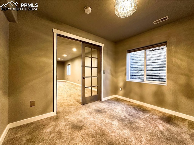 carpeted spare room featuring an inviting chandelier, a textured ceiling, and french doors