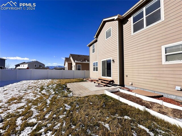 snow covered rear of property featuring entry steps, a patio area, and fence