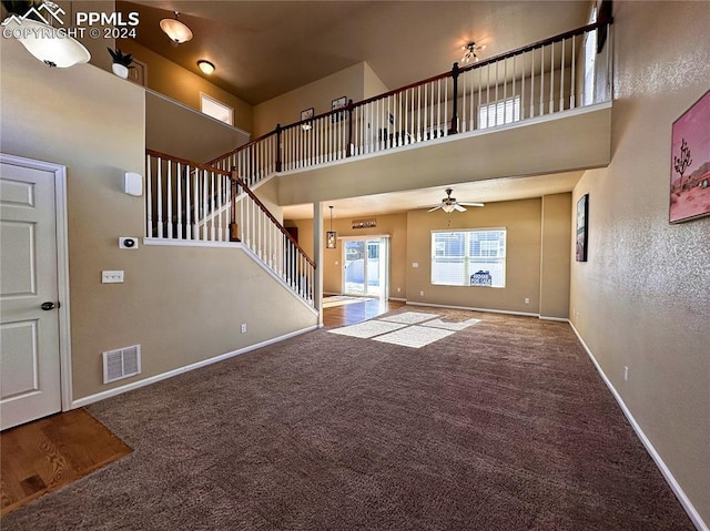 unfurnished living room with visible vents, stairway, a high ceiling, carpet flooring, and baseboards