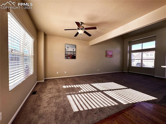 spare room featuring dark colored carpet, ceiling fan, a healthy amount of sunlight, and a textured ceiling