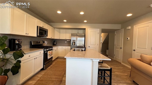 kitchen featuring light stone countertops, sink, an island with sink, white cabinets, and appliances with stainless steel finishes