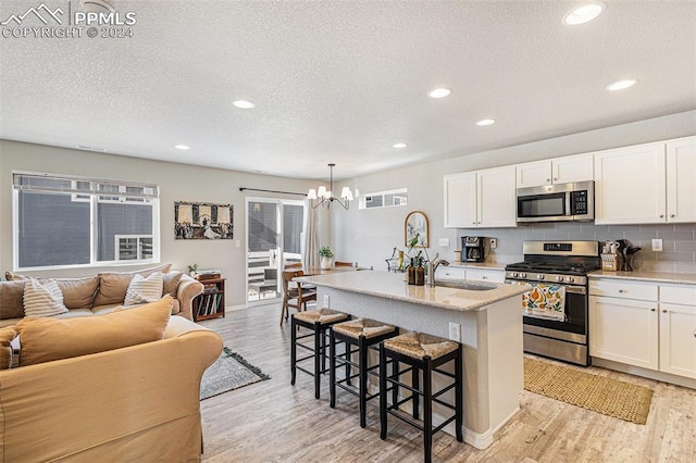 kitchen with appliances with stainless steel finishes, a kitchen breakfast bar, pendant lighting, white cabinets, and an island with sink