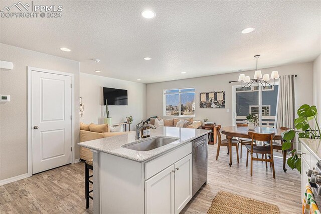 kitchen with stainless steel dishwasher, decorative light fixtures, light hardwood / wood-style flooring, white cabinets, and an island with sink