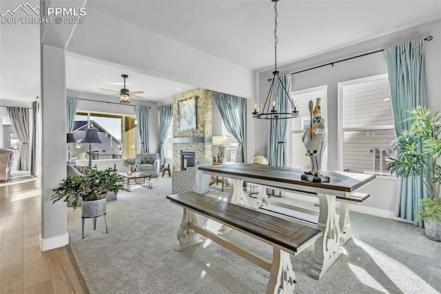 dining space with ceiling fan with notable chandelier, a stone fireplace, and carpet flooring