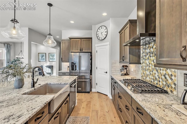 kitchen with appliances with stainless steel finishes, tasteful backsplash, wall chimney range hood, pendant lighting, and light stone counters