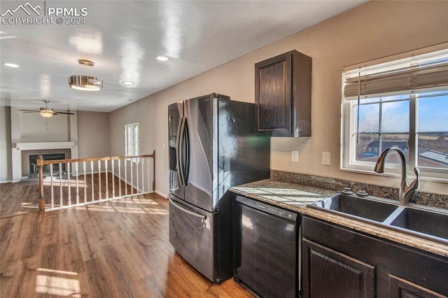 kitchen with a tile fireplace, sink, black dishwasher, dark brown cabinets, and light wood-type flooring