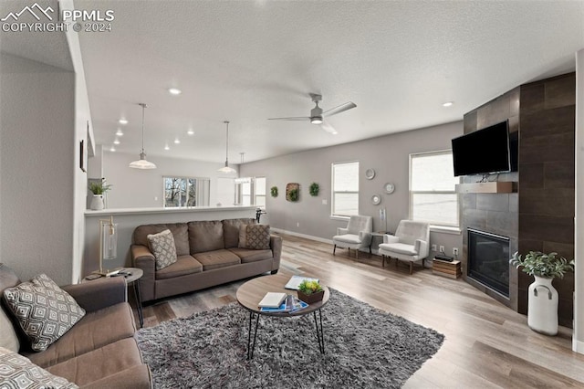 living room with ceiling fan, light hardwood / wood-style floors, a textured ceiling, and a tiled fireplace