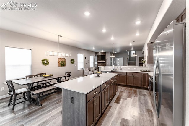 kitchen with hanging light fixtures, hardwood / wood-style flooring, a kitchen island, kitchen peninsula, and stainless steel refrigerator