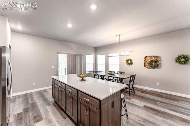 kitchen featuring a center island, stainless steel fridge with ice dispenser, hardwood / wood-style floors, pendant lighting, and a breakfast bar