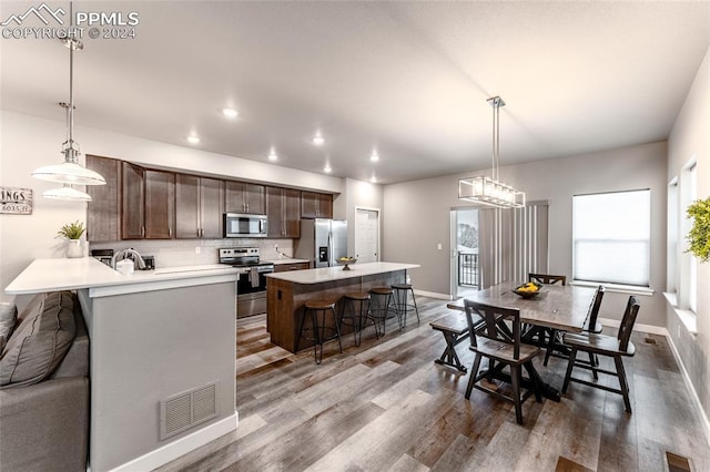 kitchen with dark brown cabinets, stainless steel appliances, hanging light fixtures, and an island with sink