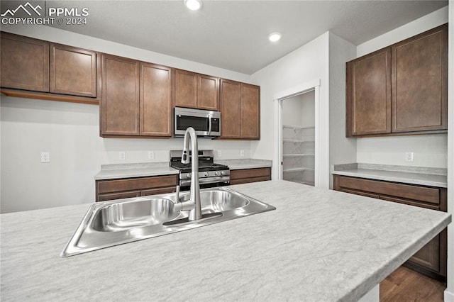 kitchen with appliances with stainless steel finishes, dark hardwood / wood-style flooring, dark brown cabinetry, and sink