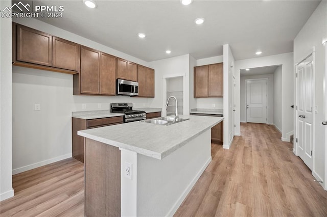 kitchen with appliances with stainless steel finishes, light hardwood / wood-style floors, a kitchen island with sink, and sink