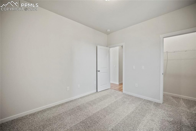 unfurnished bedroom featuring carpet flooring, a walk in closet, and a closet