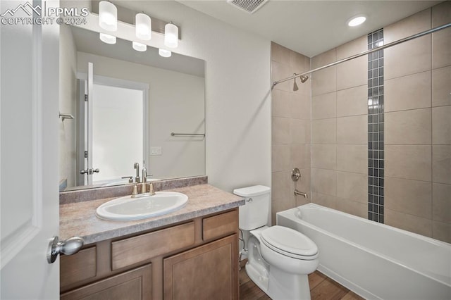 full bathroom with hardwood / wood-style flooring, tiled shower / bath combo, vanity, and toilet