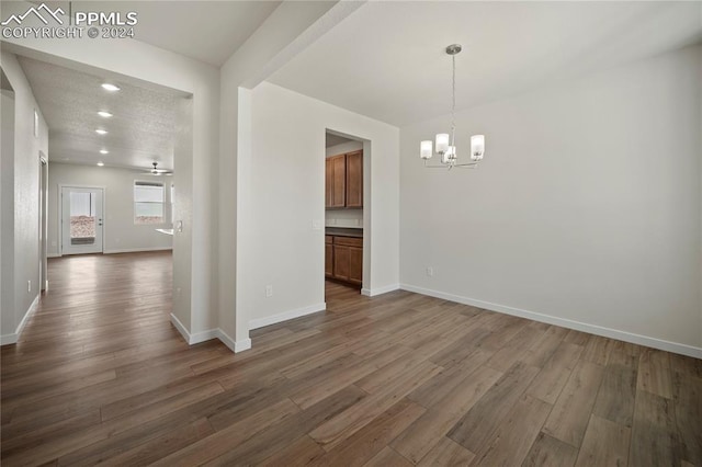 unfurnished dining area featuring a textured ceiling, dark hardwood / wood-style flooring, beam ceiling, and ceiling fan with notable chandelier