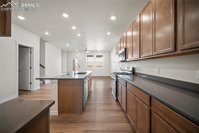 kitchen featuring ceiling fan, a center island with sink, sink, light wood-type flooring, and appliances with stainless steel finishes