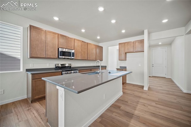 kitchen with sink, appliances with stainless steel finishes, light hardwood / wood-style flooring, and a kitchen island with sink