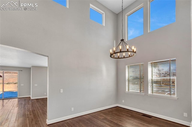 empty room featuring a high ceiling, a healthy amount of sunlight, dark hardwood / wood-style floors, and an inviting chandelier