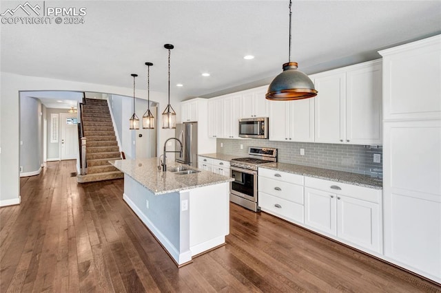 kitchen with hanging light fixtures, stainless steel appliances, dark hardwood / wood-style floors, and a kitchen island with sink